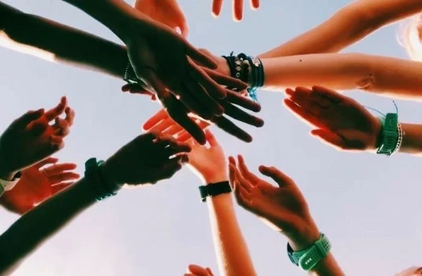 Teen athletes stacking hands in a team huddle before practice, viewed from below against the sky